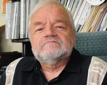 David, an older gentleman with silver hair and beard, sits in a chair and looks into the camera