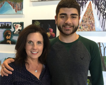 John, a young man with dark hair and beard poses with his Mom, Eileen. John has his arm around his mom’s shoulder and both smile