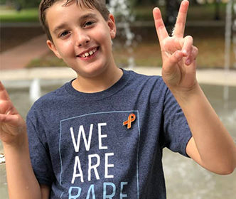 Franco smiles into the camera and holds peace signs up with both hands, his shirt reads “We Are Rare”