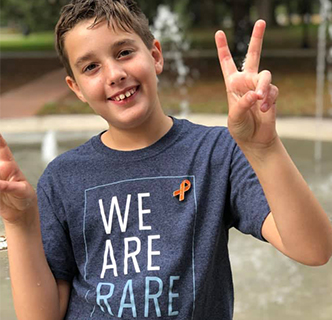 Franco smiles into the camera and holds peace signs up with both hands, his shirt reads “We Are Rare”